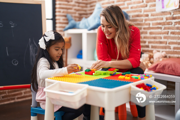 Teacher and toddler playing with construction blocks sitting on table at kindergarten