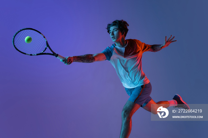 Young caucasian man playing tennis isolated on purple-blue studio background in neon, action and motion concept