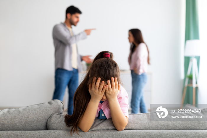 Family crisis. Little girl crying, closing face with hands while her angry parents fighting on the background