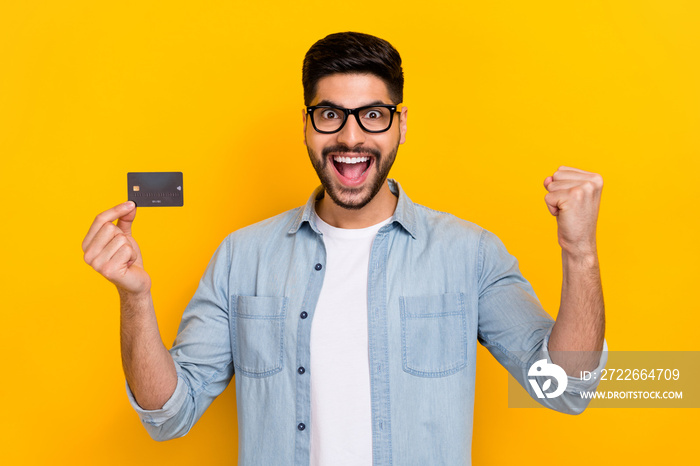 Closeup photo of young celebrating guy holding new bank card will buy everything want shopaholic isolated on bright yellow color background