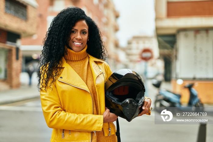 Middle age african american woman holding motorcycle helmet at the city.