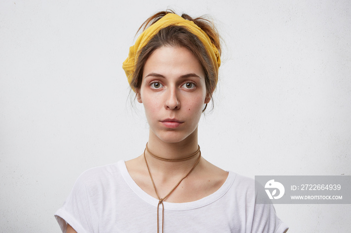 Attractive female with dark eyes, thin lips and healthy pure skin having serious expression looking directly into camera isolated over white wall of studio. Confident female with European appearance