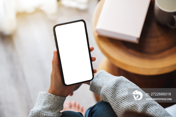 Top view mockup image of a woman holding mobile phone with blank desktop screen while sitting in bed room at home