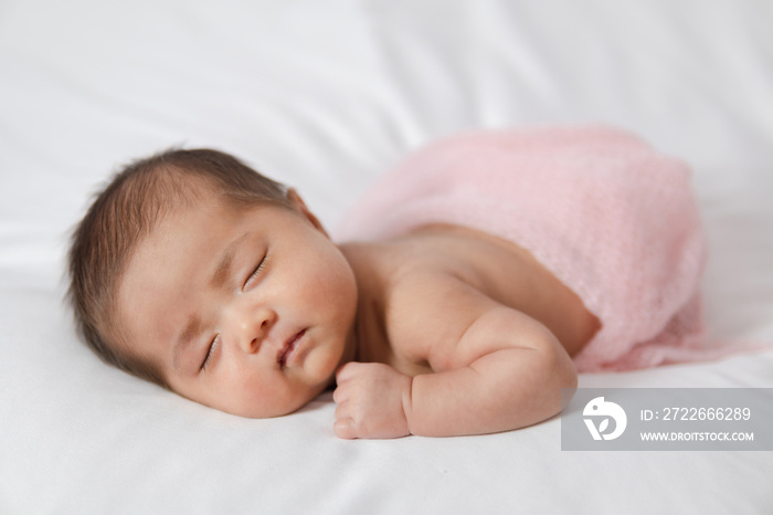 Adorable asian newborn baby in pink wrap sleeping on white blanket background.