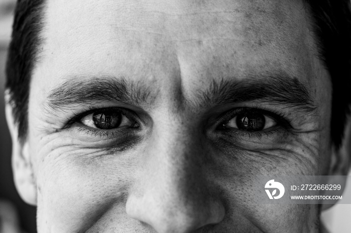 Fragment of a man’s face: an eyes and nose to compile an identikit. Fragment of the wrinkled face of a young guy. Smiling eyes of a man. Black and white photo.