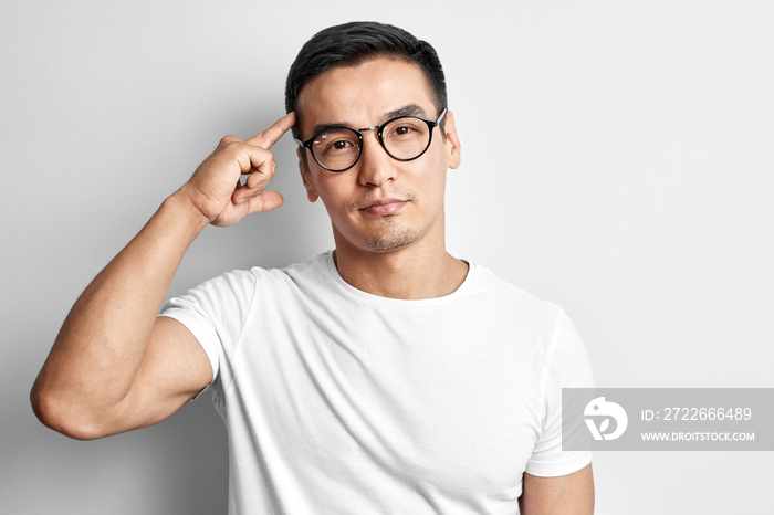 Portrait of smart thinking Kazakh man in glasses dressed in casual points finger at head and brain, has idea on white background. Asian handsome genius demonstrates his mind