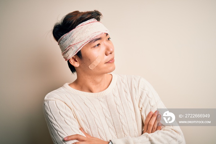 Young handsome chinese man injured for accident wearing bandage and strips on head looking to the side with arms crossed convinced and confident