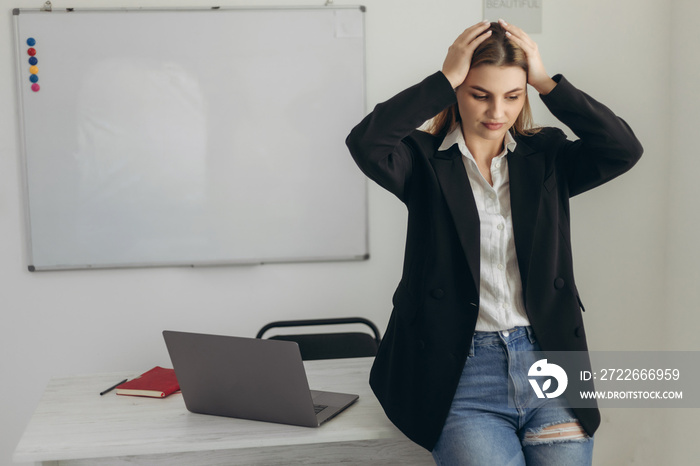 Portrait of a worried teacher holding her head. The girl is wearing a white shirt and a black jacket