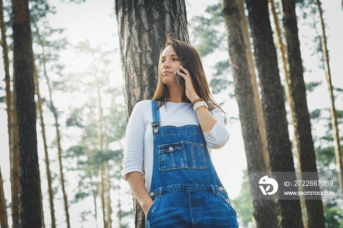 Beautiful young woman in denim overalls in forest