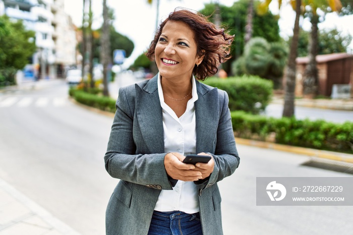 Middle age latin businesswoman smiling happy using smartphone at the city.