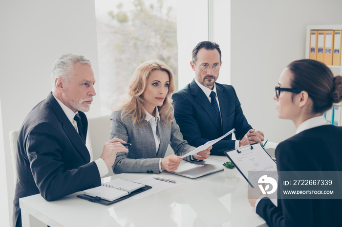 Portrait of young attractive woman in glasses having job interview with three stylish business persons in financial company, asking, answering the questions, holding cv in hands