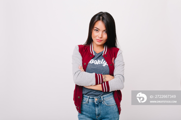 Indoor portrait of charming asian girl with tattoo under jacket sleeve. Cute dark-haired female student in bomber posing with arms crossed isolated on white background.