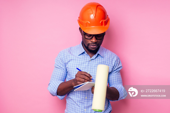 black man African American holding paint roller in hand paints the wall in pink color .happy african builder painting inside the house,businessman wears a helmet hard hat.young guy is painting