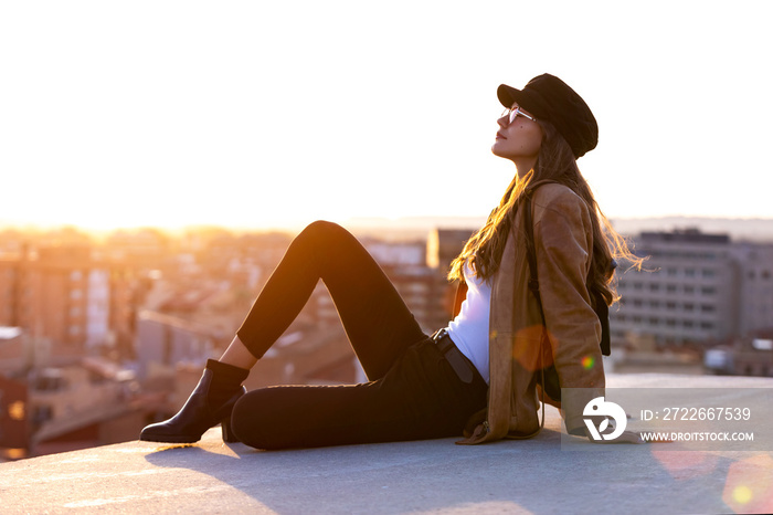 Pretty young woman enjoying time and sunset while sitting on the rooftop.