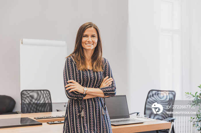 Stylich attractive young woman in the office. Businesswoman with folded arms standing at the table