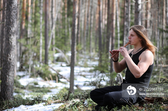 A musician with a tool in nature. A man is playing a flute in a pine forest. The music of the druids in the spring forest.