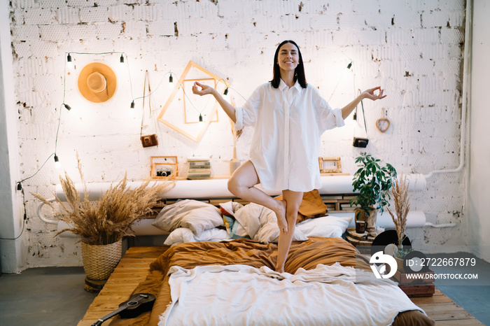 Cheerful woman standing on bed on one leg