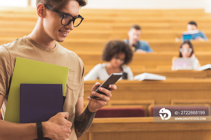 Cheerful modern male student messaging on mobile phone