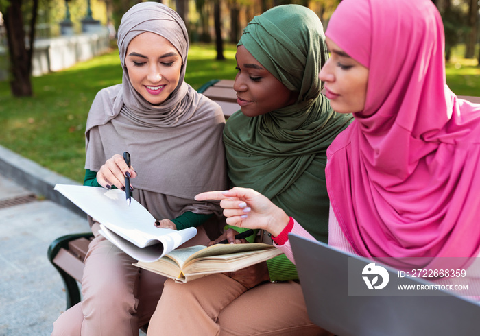 Three Muslim Females Students Learning Together Sitting On Bench Outside