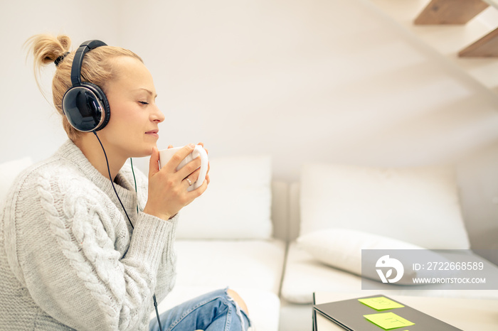 Young woman listening to music and enjoying cup of coffee