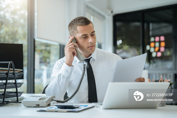 Asian Businessman sitting in office using a cellphone and laptop.