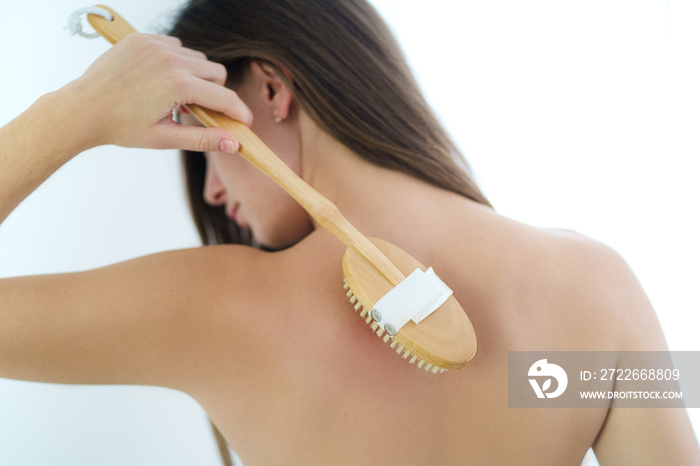 Woman brushing back with a dry wooden brush to prevent and treatment body problem after shower at home. Skin health