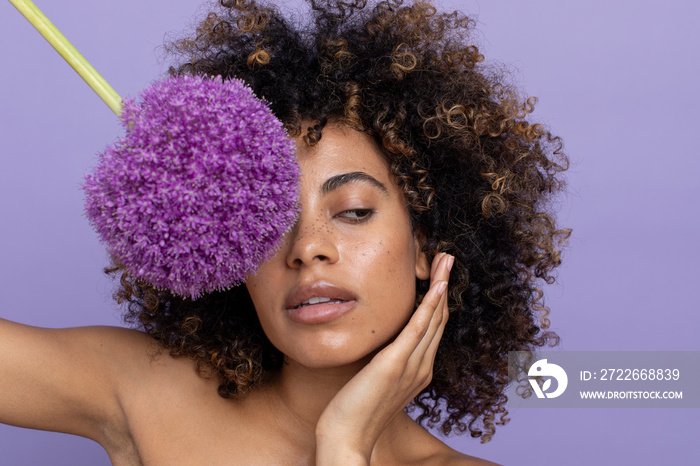 Brunette woman covering eye with purple flower