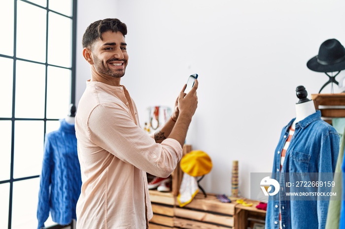 Handsome hispanic man shopping at retail shop taking pictures of clothes at retail shop