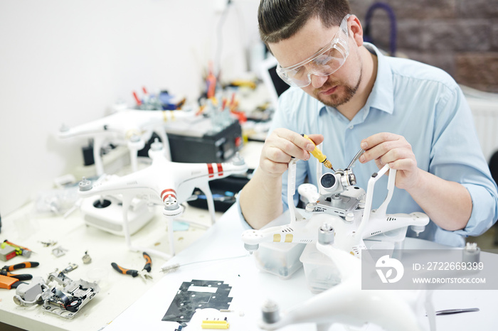 Portrait of modern man working on assembling several high tech drones and attaching cameras in electronics workshop