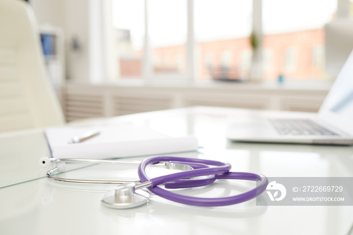 Focus on modern stethoscope with purple rubber tube placed on doctors table in office full of light