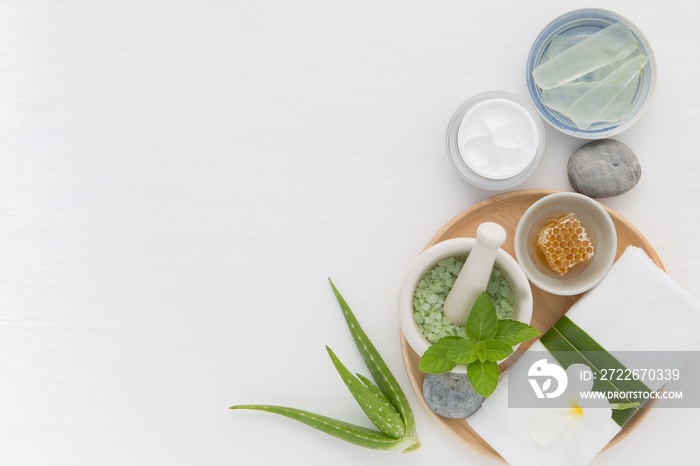 Homemade skin care and body scrub with natural ingredients honey, salt, mint, natural lotion and aloe vera set up on white wooden background.