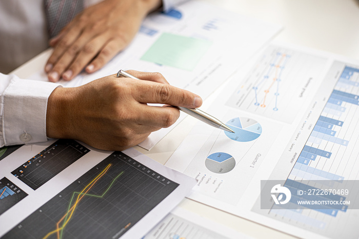 A businessman pointing at a document with a pen to check the financial numbers, he is sitting in his private office, the businessman examining the financial data from the corporate finance chart.