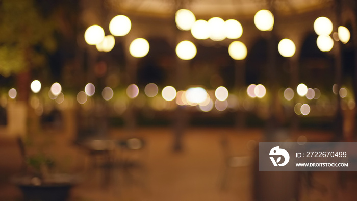 Bokeh shot of urban park with street lamps and cafe style tables