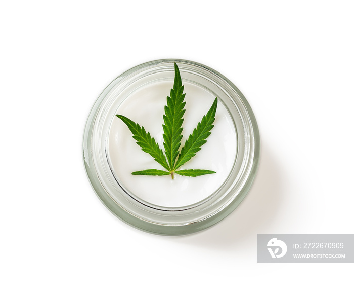 Moisturizing skin care cream and green cannabis sativa leaf in a glass jar isolated on a white background. Hemp cosmetics concept. Medical marijuana plant for herbal face and body care.