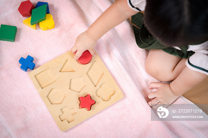 An adorable preschool little girl 2-3 years in Montessori classroom engaged sensory wooden shape and color blocks. Educational toys, Cognitive skills, Child development, Learn through play concept.