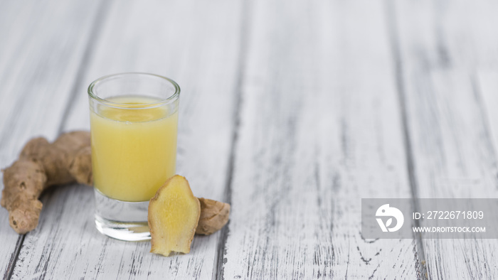 Old wooden table with fresh Ginger Juice (close-up shot; selective focus)