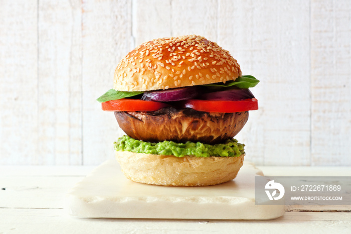 Portobello mushroom meatless burger with avocado, tomato, spinach and onion on a marble serving board against a white wood background