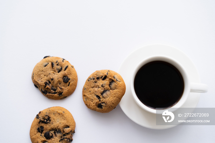 top view of cup of coffee near chocolate chip cookies on white.