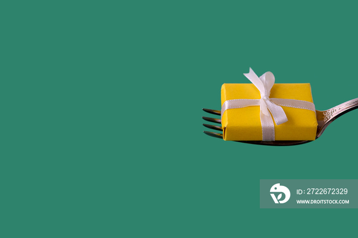 yellow gift with white ribbon lies on fork on green background. holiday, christmas or birthday concept. copy space,