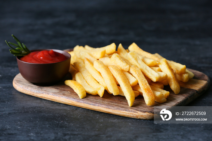 Wooden board with tasty french fries and ketchup on black background