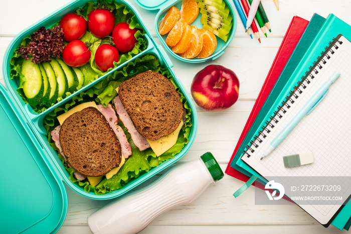 School lunch box with sandwiches and fruit vegetables and school supplies: the concept of a healthy and balanced diet