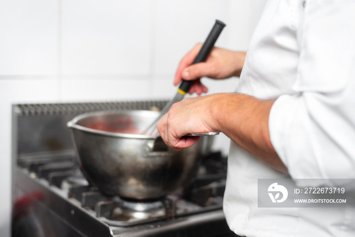 Pastry Chef in the kitchen cooking a red strawberry marmalade cream .