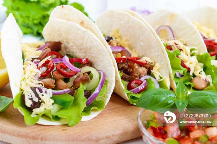 Tacos is a traditional Mexican dish. Tortilla stuffed with chicken, bell and hot peppers, beans, lettuce, cheese, blue onion with salsa sauce on white wooden background.