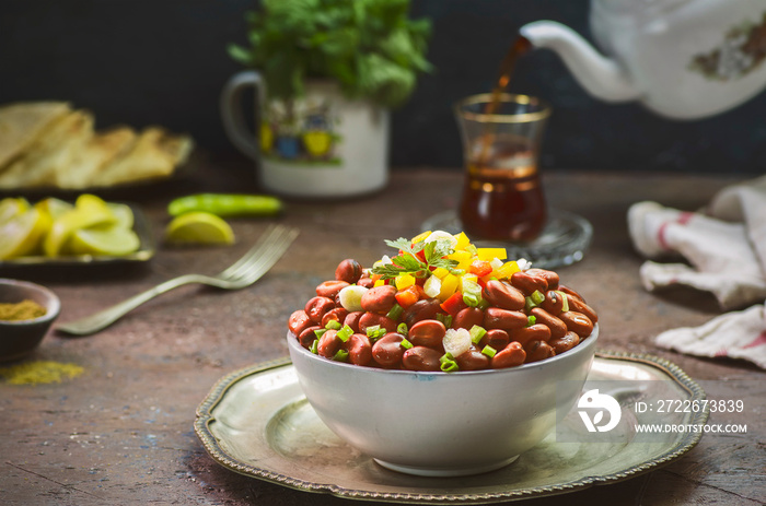 Arabic cuisine; Egyptian traditional dish  Ful Medames .Middle Eastern delicious breakfast with cooked Fava beans topped with fresh ingredients. Teapot pouring tea into a cup in the background.