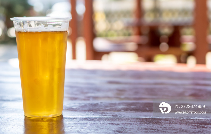 beer in a plastic mug on a brown table with a blurry background