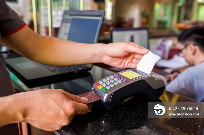 Hand put credit card In slot of credit card reader and pull slip with blurry cashier and laptop at counter service, credit card payment, buy and sell products & service, the concept of payment.