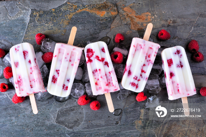 Group of raspberry vanilla yogurt ice pops. Above view in a row on a dark slate background.
