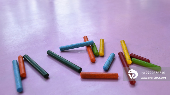 Many old colored crayon placed on a pink wood table.