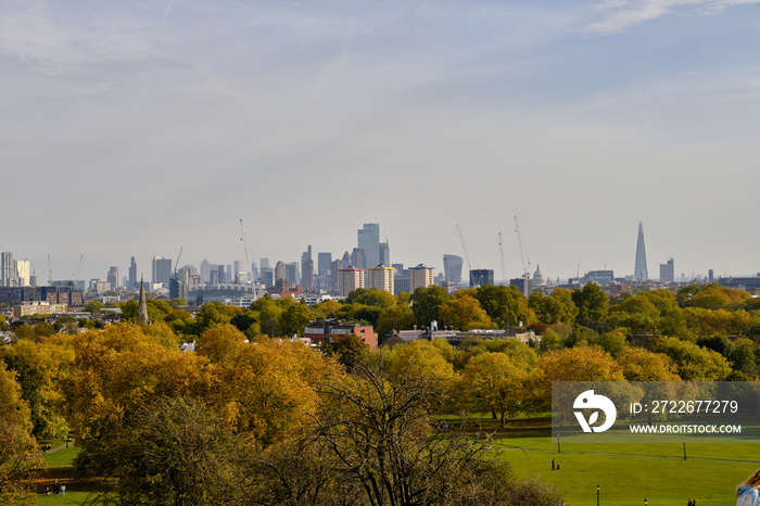 London skyline viewed from Primrose Hill with autumnal trees and cloudy sky.