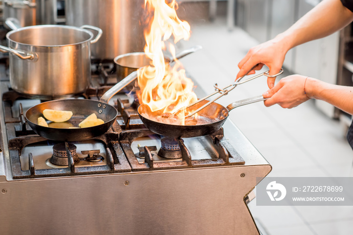 Chef frying meat steak on the gas stove with fire at the kitchen. Close-up view on the frying pan